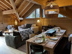 A wooden interior with a dining table set for four, a sofa, and a hanging light fixture. - Modern apartment with parking - 8 guests (Arâches-la-Frasse)