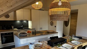 Una cucina moderna con isola centrale, una zona pranzo con un tavolo lungo apparecchiato per sei persone e un soffitto con lampade intrecciate.