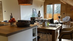 Una cucina moderna con isola in legno, zona pranzo con sedie e un'ampia finestra che si affaccia su un patio in legno.