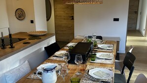 Un tavolo da pranzo apparecchiato con piatti, bicchieri e una griglia, in una stanza con pavimento in legno e un lampadario.