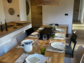 A dining table set with plates, glasses, and a grill, in a room with a wooden floor and a hanging light fixture. - Modern apartment with parking - 8 guests (Arâches-la-Frasse)