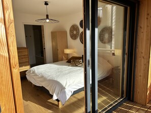 A bedroom with a bed, a nightstand, a lamp, and a sliding glass door leading to a balcony. - Modern apartment with parking - 8 guests (Arâches-la-Frasse)
