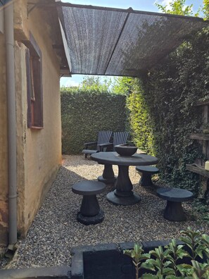 Une terrasse extérieure avec une table et des chaises, entourée de gravier et de verdure.