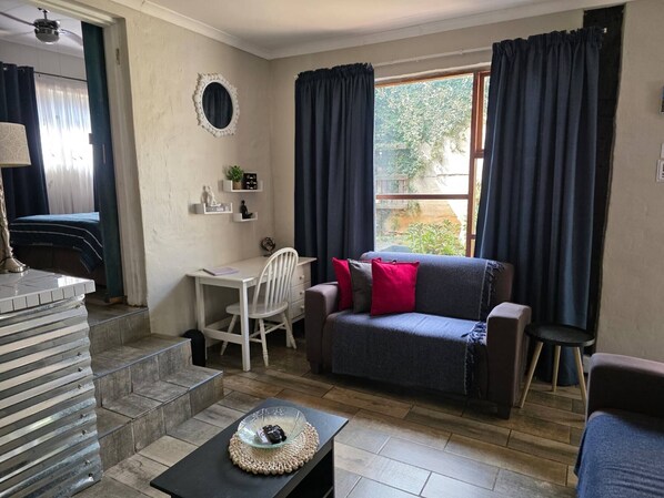 Une pièce comprenant un canapé, un bureau, une chaise, une petite table avec un saladier en verre et une fenêtre avec des rideaux.