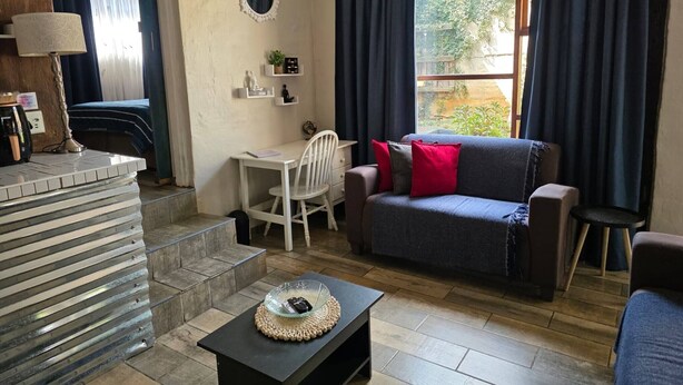En stue med sofa, bord, kaffemaskine, lampe, et lille planter og et vindue med gardiner.