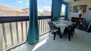 Un balcon avec une table à manger pour deux personnes, un rideau bleu et une vue sur les immebles.