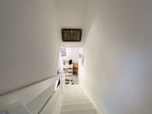 Un escalier menant à une pièce où se trouvent un bureau et une chaise, un certificat encadré accroché au mur, et un tableau d’affichage recouvert de feuilles de papier.