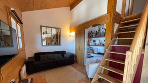 Een gezellige woonkamer met houten plafond, een bank, een salontafel, een televisie, een trap en een boekenkast.