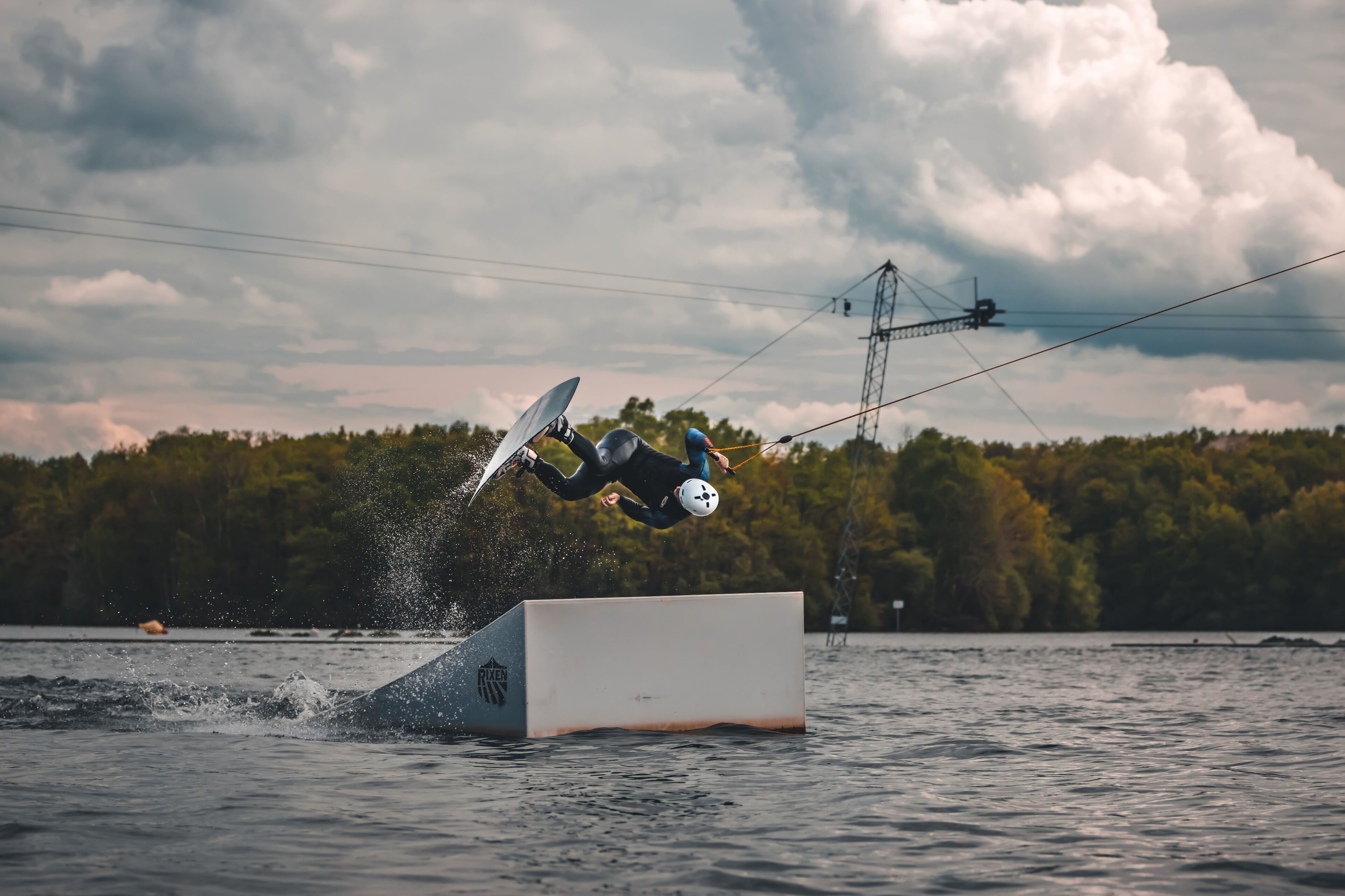 A person performing a wakeboarding trick over a ramp.