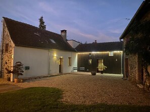 A building with a gravel courtyard, a stone wall, and a wooden structure with lights.