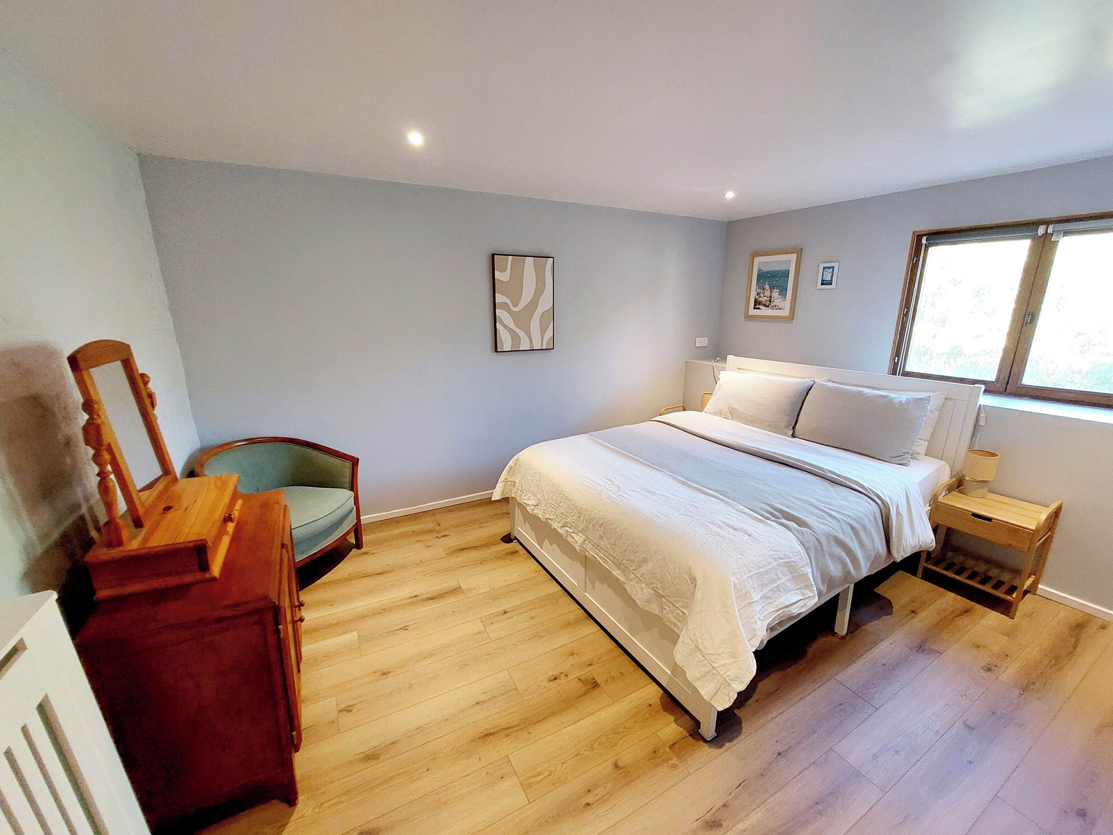 Een slaapkamer met een bed, een stoel, een nachtkastje en een raam.