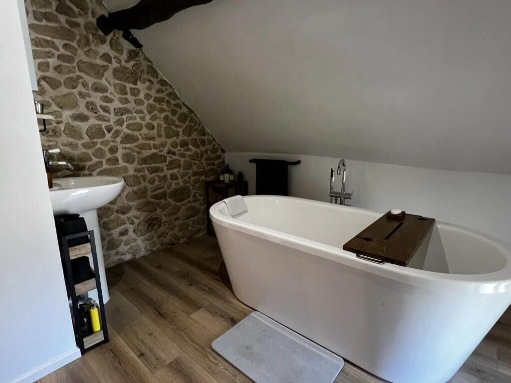 A bathroom with a stone wall, a white bathtub, a sink, and a wooden shelf.