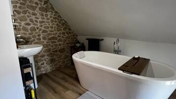 A bathroom with a stone wall, a white bathtub, a sink, and a wooden shelf.