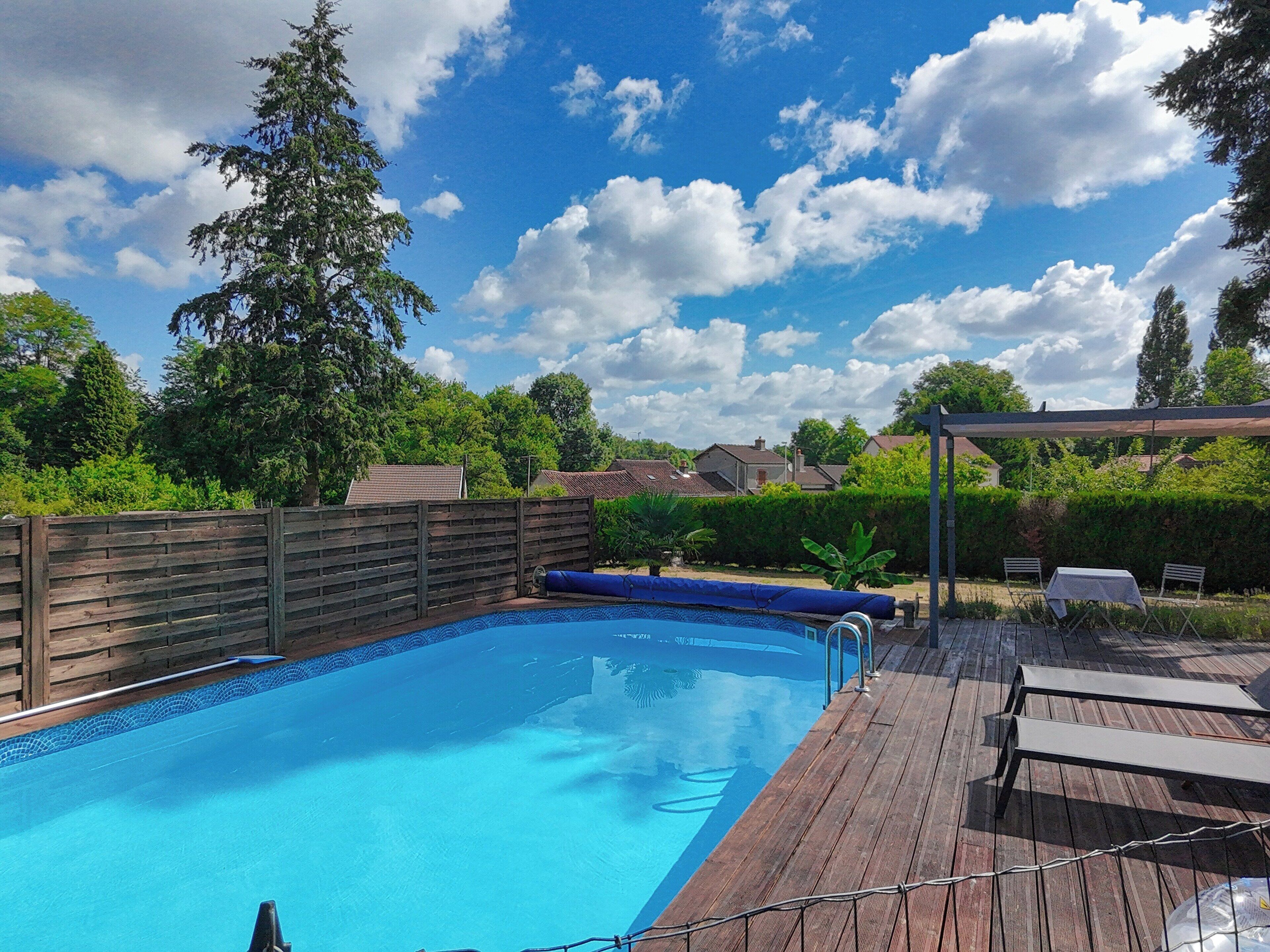 A swimming pool with a wooden deck, surrounded by a wooden fence and trees.
