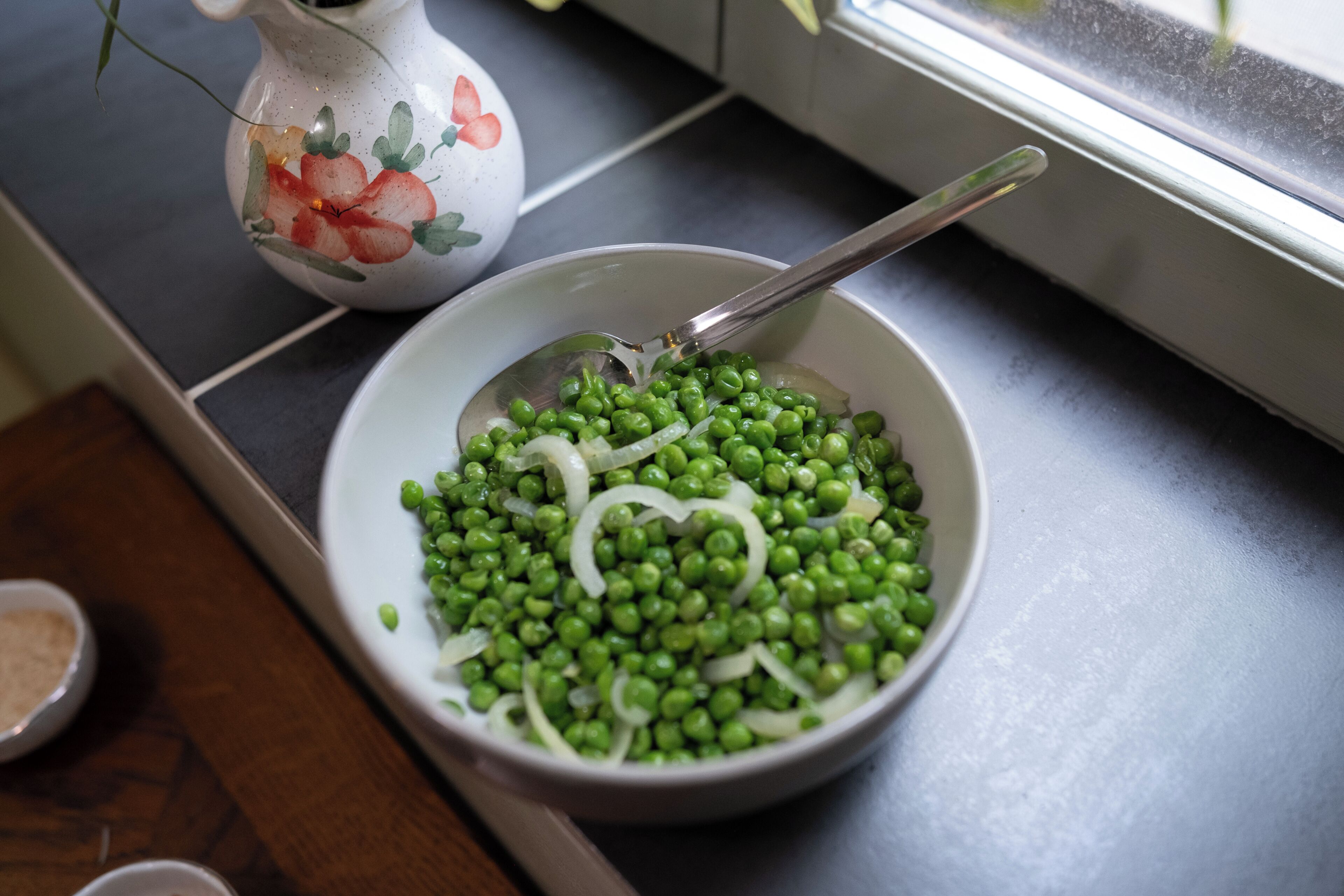 Een schaal groene erwten met uien op een aanrecht.