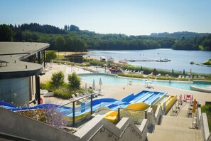A swimming pool area with multiple pools, a beach, and a lake view. - Bluedothotel France (Magnac-Laval)