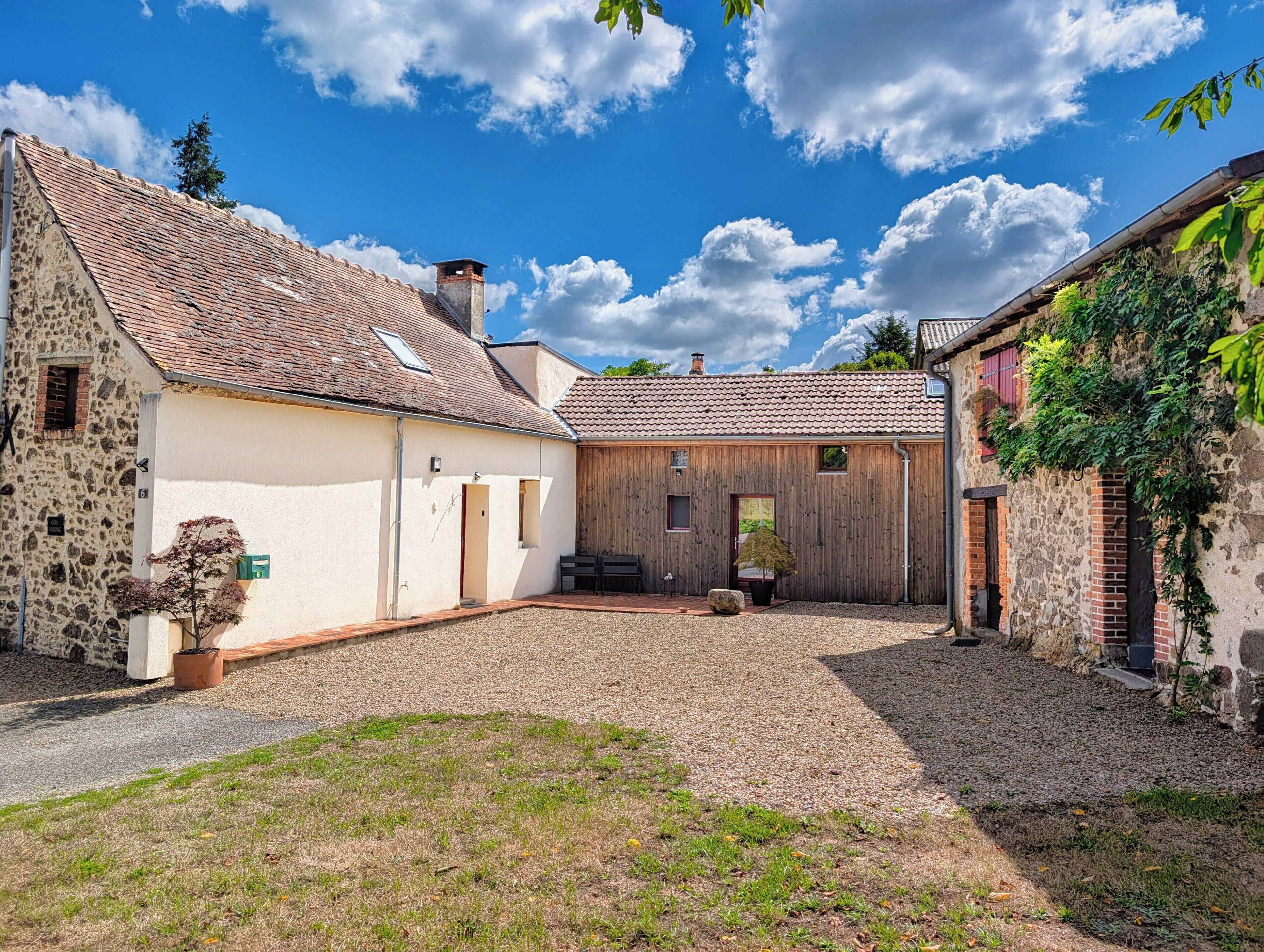 A courtyard with a stone building, wooden structure, and a gravel path.