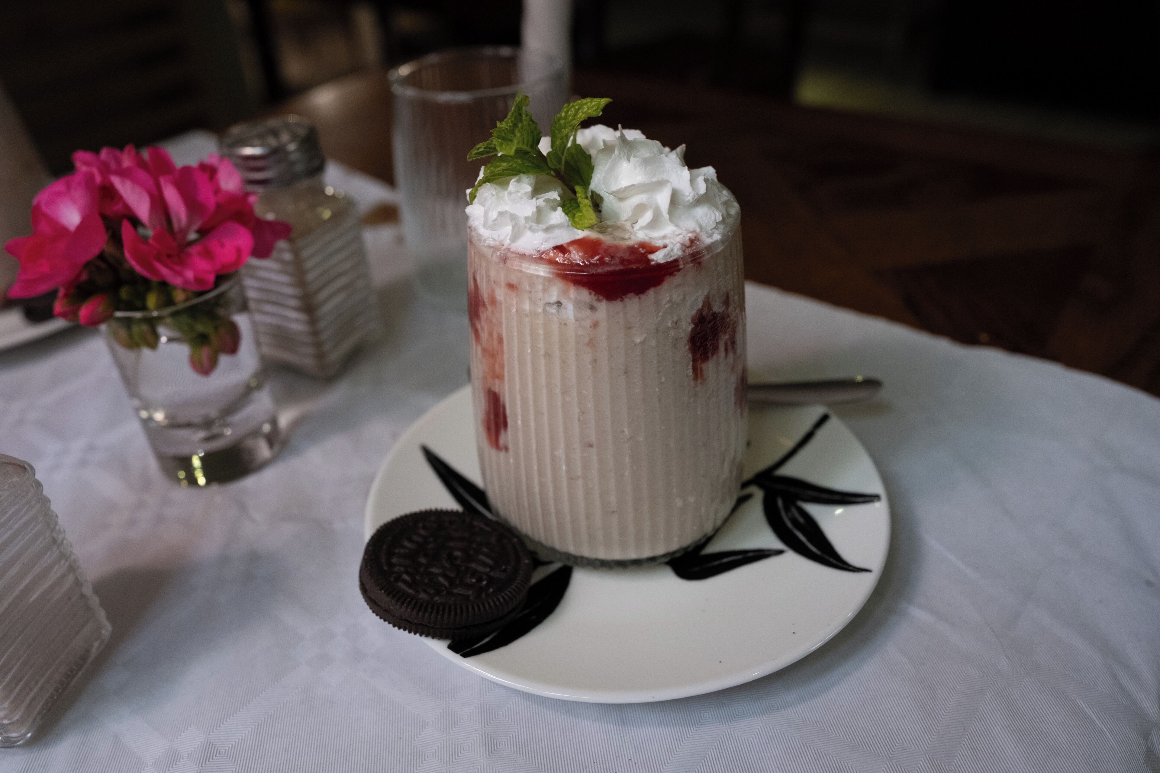 A dessert on a white plate with a mint garnish, surrounded by a white tablecloth.