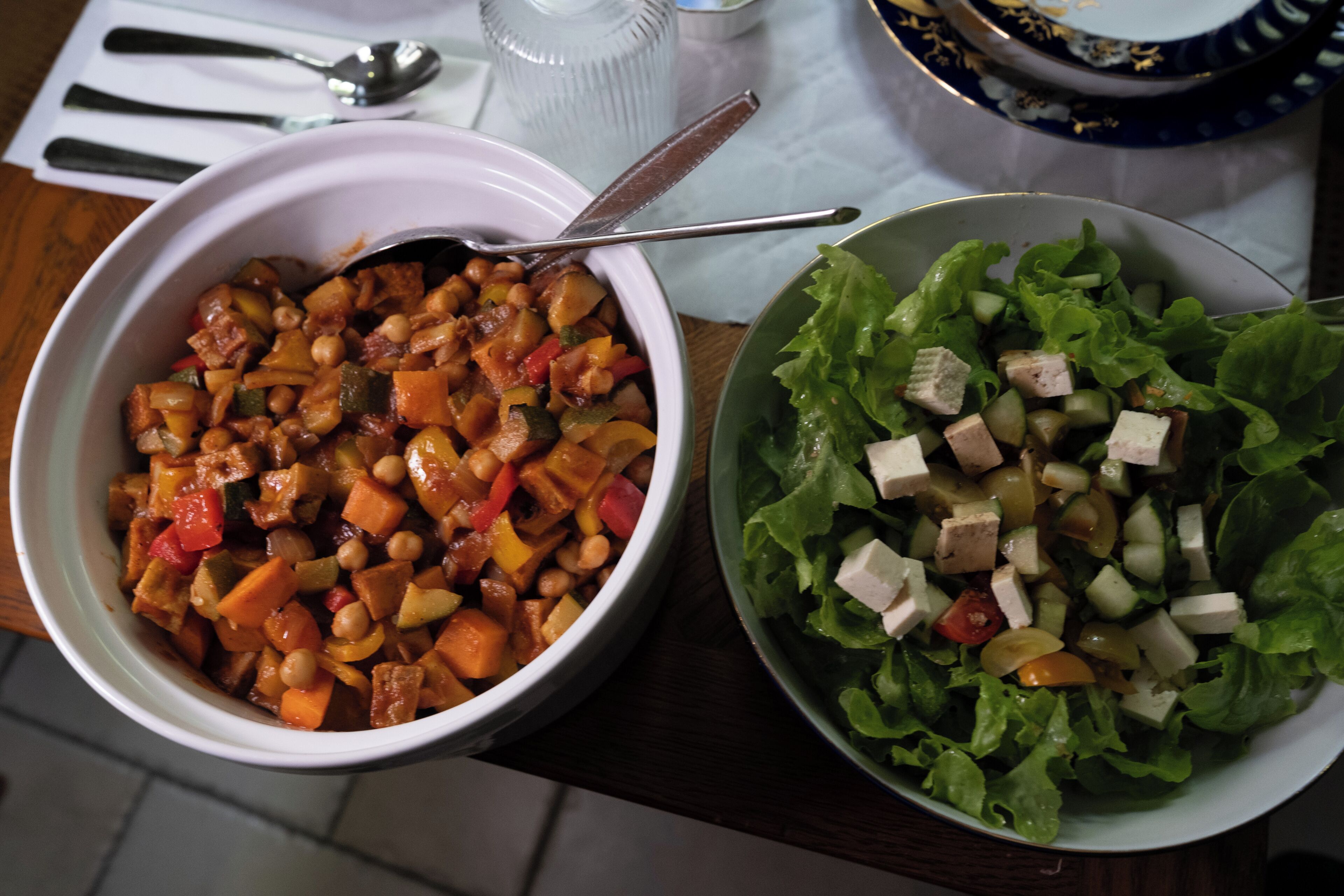 Two bowls of food on a table with a spoon and a glass.