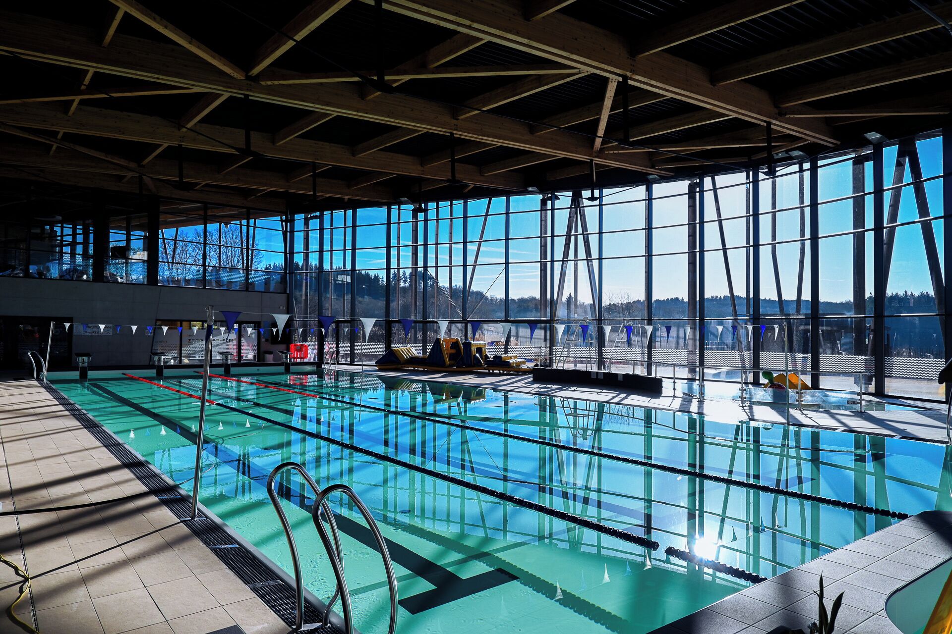 An indoor swimming pool with clear glass walls, a tiled floor, and a view of the outdoors.