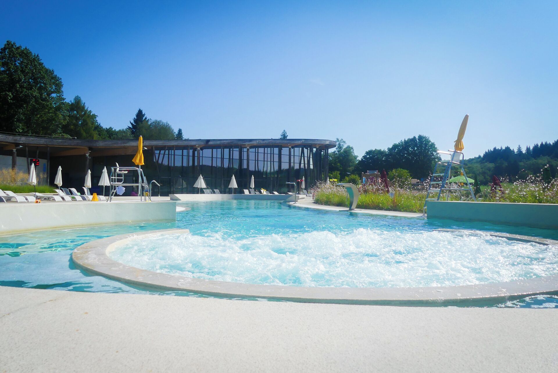 A swimming pool with a water feature, lounge chairs, and a covered area with umbrellas.