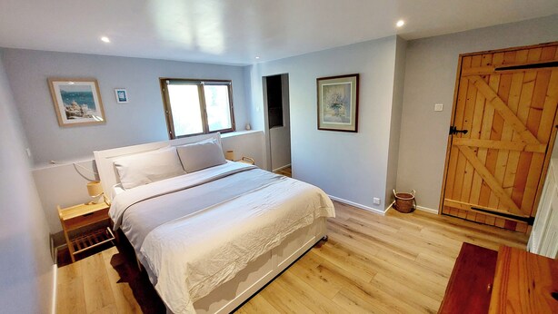 A bedroom with a bed, a wooden floor, a wardrobe, and two windows.