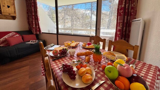 Et spisebord med dug i tern, forskelligt frugt, brød og en kniv.