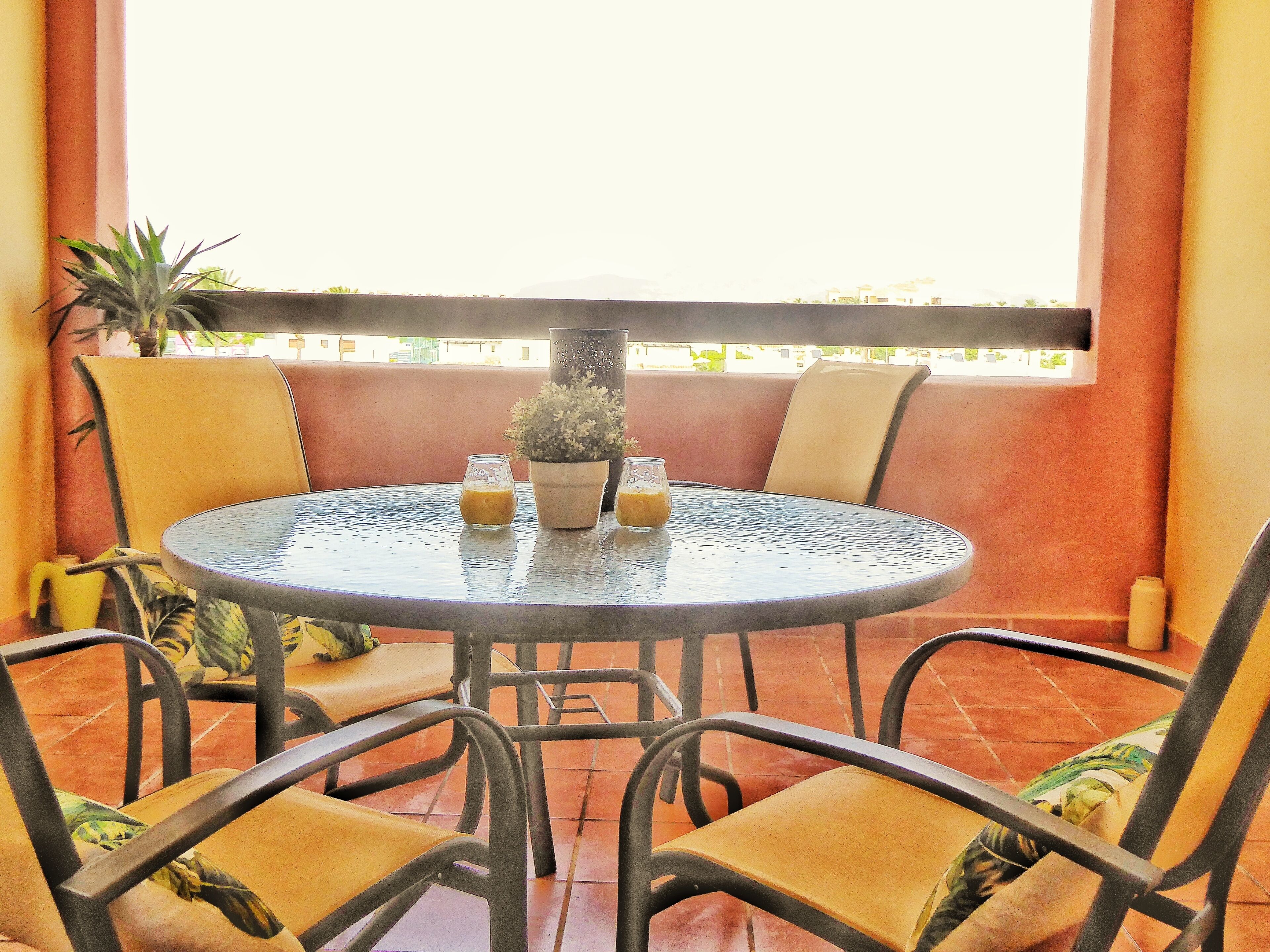 Une table ronde avec des chaises, une plante en pot et deux verres de jus d’orange.