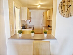 A compact kitchen with a sink, stove, and cabinets, a clock on the wall, and two potted plants on the counter. - Mar Menor Golf 2 Free Gym Padel Tennis Pool (MC)
