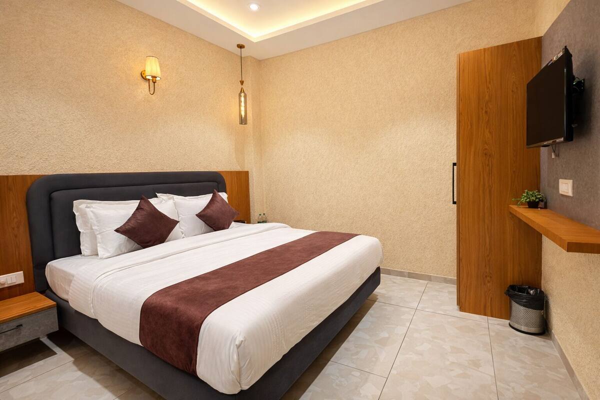 A modern hotel room with a large bed, a TV mounted on the wall, and a small shelf with a plant.