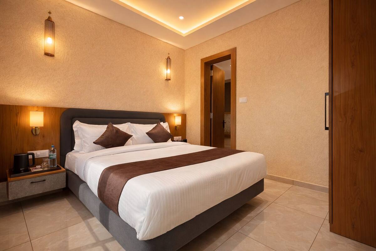 A hotel room with a large bed, bedside tables, a wooden wardrobe, and wall-mounted lighting.
