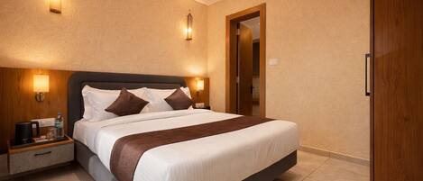 A hotel room with a large bed, bedside tables, a wooden wardrobe, and wall-mounted lighting.