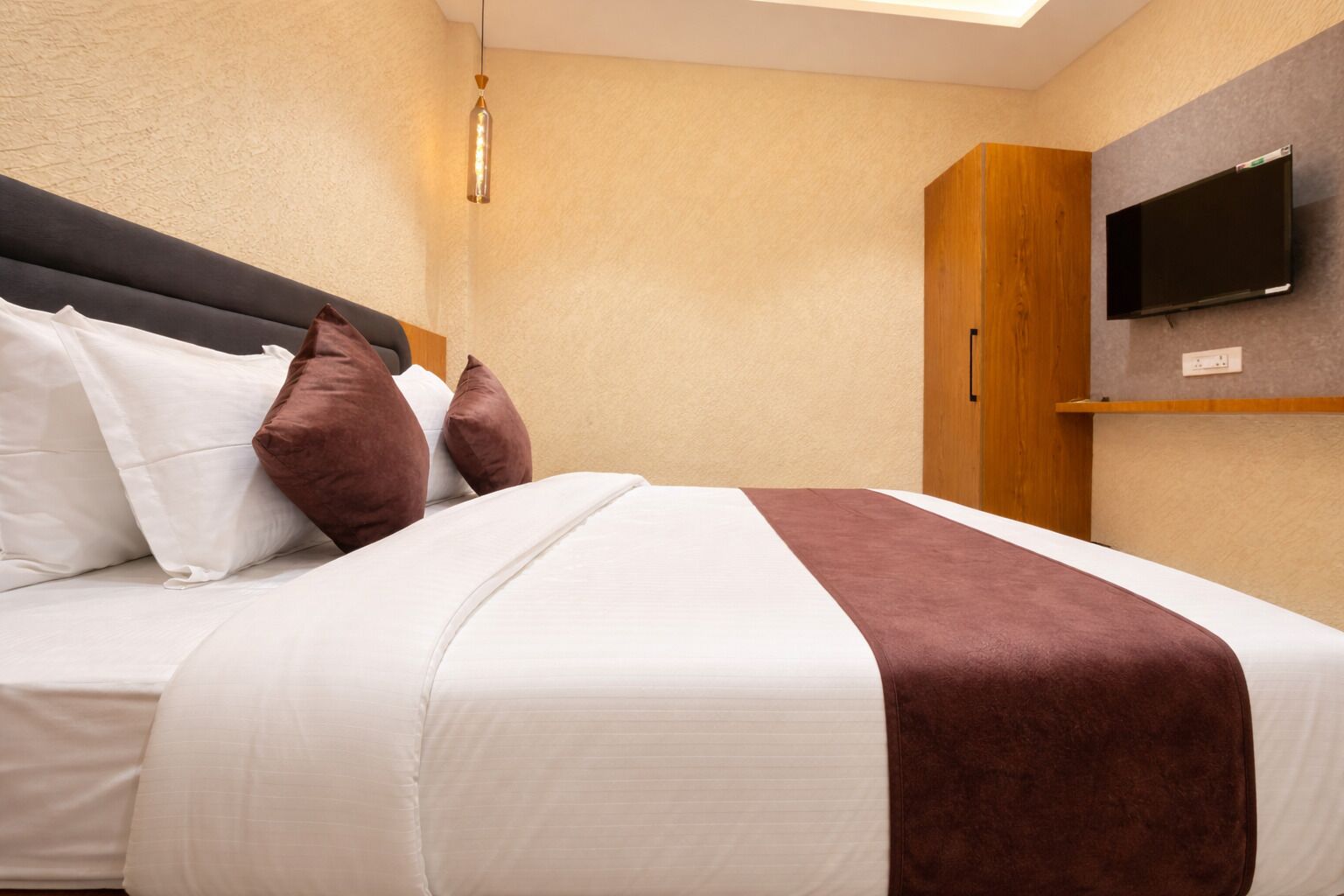 A hotel room with a bed, pillows, a TV, and a wooden wardrobe.