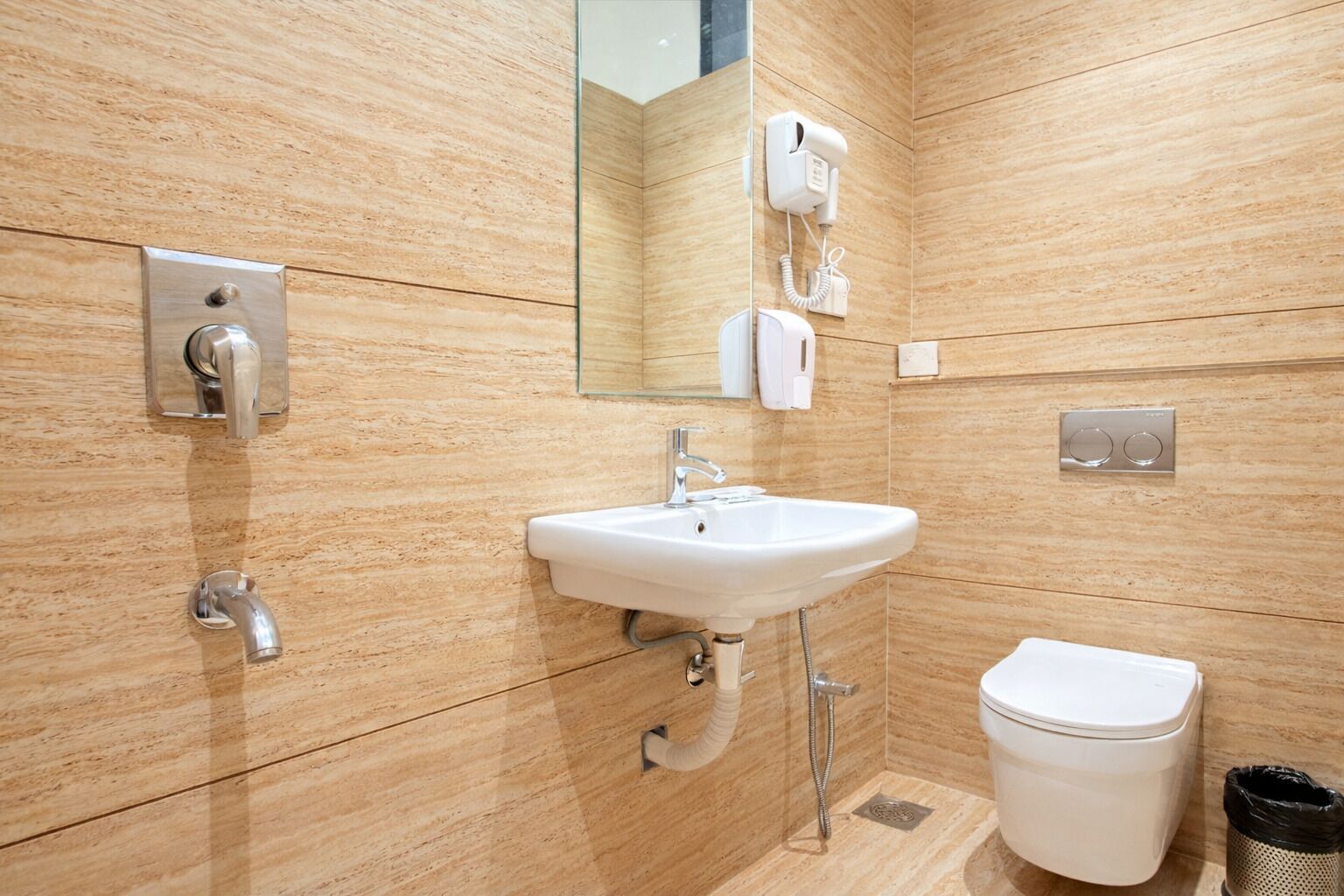 A modern bathroom with a sink, mirror, toilet, and a hairdryer mounted on the wall.