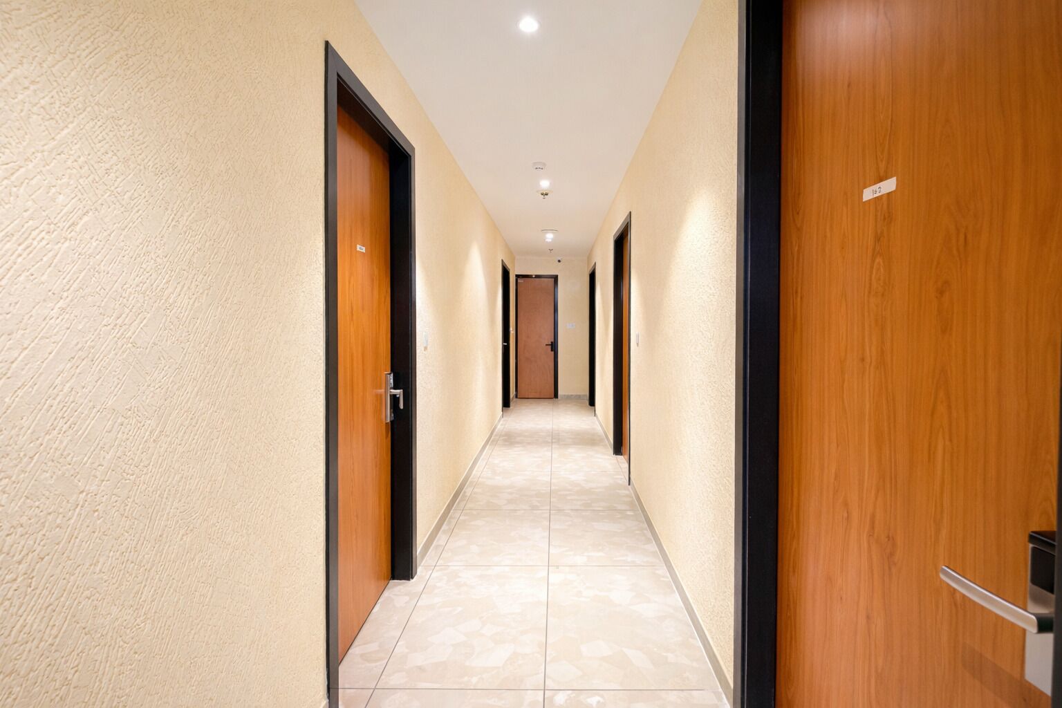 A hotel hallway with wooden doors, beige walls, and tiled flooring.