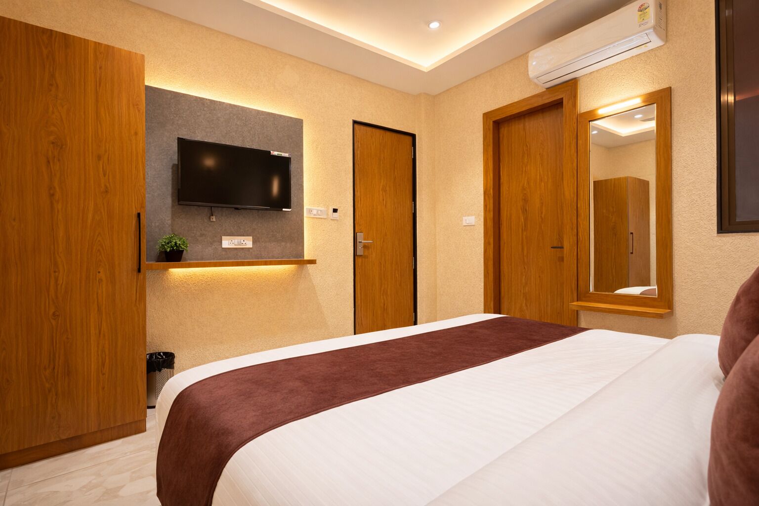 A hotel room with a bed, a mounted TV, a mirror, and wooden wardrobes.