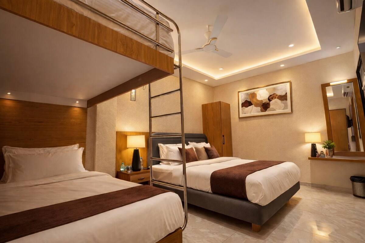 A hotel room with bunk beds, a ceiling fan, a bedside table with a lamp, a framed artwork, and a mirror.