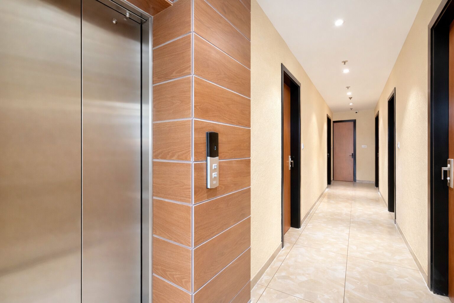 En gang med en moderne elevator, et intercomsystem på væggen og flere døre.