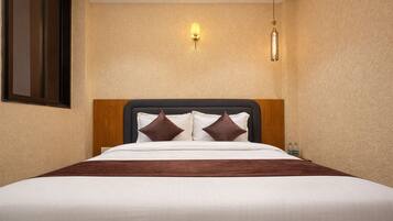 Habitación de hotel con cama, dos lámparas fijadas a la pared y cabecero de madera.