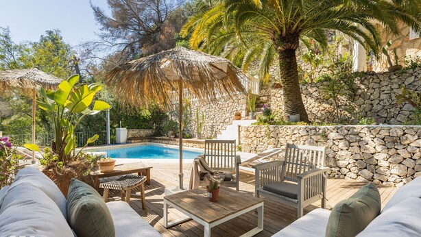 A poolside area with a wooden deck, lounge chairs, a table, and a stone wall. - Villa MAGIA by Abahana Villas (Benissa)