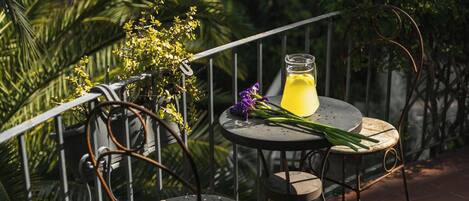 A balcony with a round table, a metal chair, a glass bottle, and a purple flower.