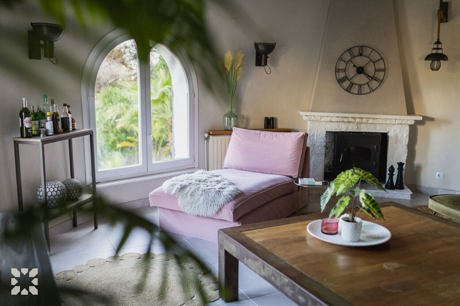 A cozy living room with a pink sofa, a fireplace, and a large window with a view of greenery.