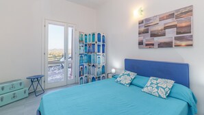 Ein Schlafzimmer mit einem Bett, einem Wandbild, einem Nachttisch und Blick durch eine Tür.