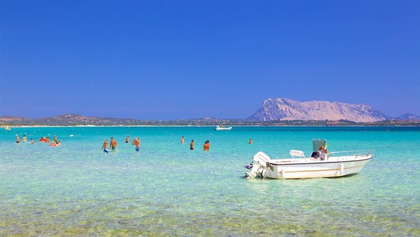 Ein Strand mit klarem türkisblauem Wasser, einem Boot und fernen Bergen.