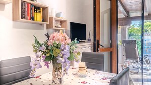 Ein Essbereich mit einem Tisch für zwei Personen, einem Blumenstrauß, einem Fernseher und einem Bücherregal mit Büchern.