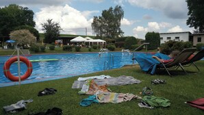 Piscina com boia salva-vidas, cadeiras de descanso e objetos espalhados na grama.