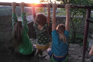 Trois enfants sont suspendus Ă une structure en bois, Ă lâextĂ©rieur.
