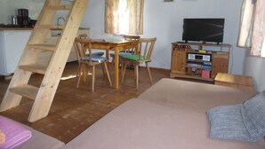 Um quarto aconchegante com uma escada de madeira, uma mesa de jantar com cadeiras, um sofá, uma televisão e uma área de cozinha ao fundo.
