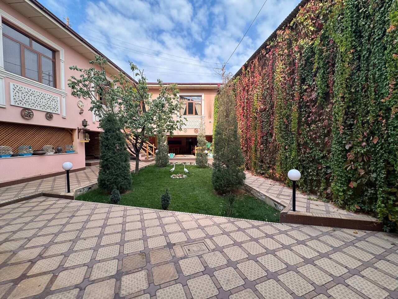 A courtyard with a tiled floor, a small lawn, and a wall covered in ivy.