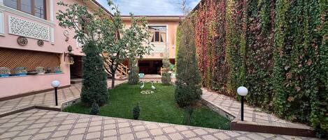 A courtyard with a tiled floor, a small lawn, and a wall covered in ivy.